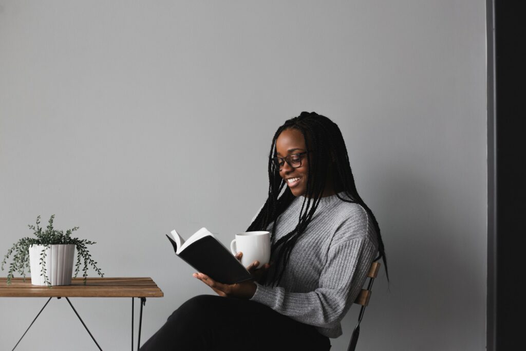 Woman with a growth mindset reading a book at a table holding mug.