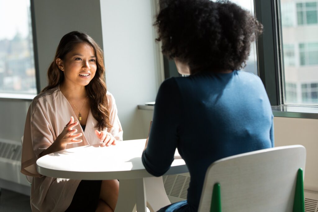 Two professional women meeting as a form of networking at a table in an office setting.